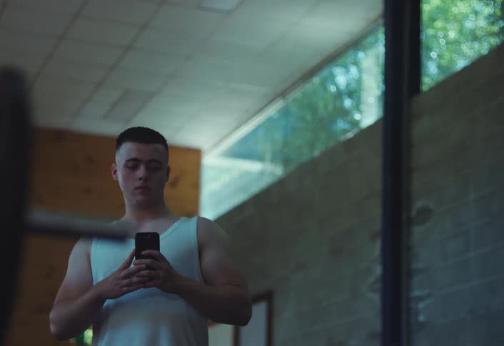 Young man takes a mirror selfie while standing in a room near a weight bar