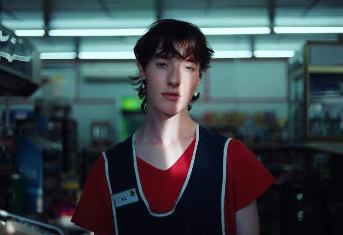A teen wearing a red tshirt and a blue vest is posing for the camera while in a warehouse