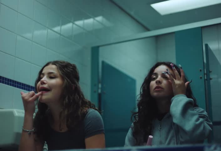 Teenage girls apply makeup at a mirror in a public bathroom