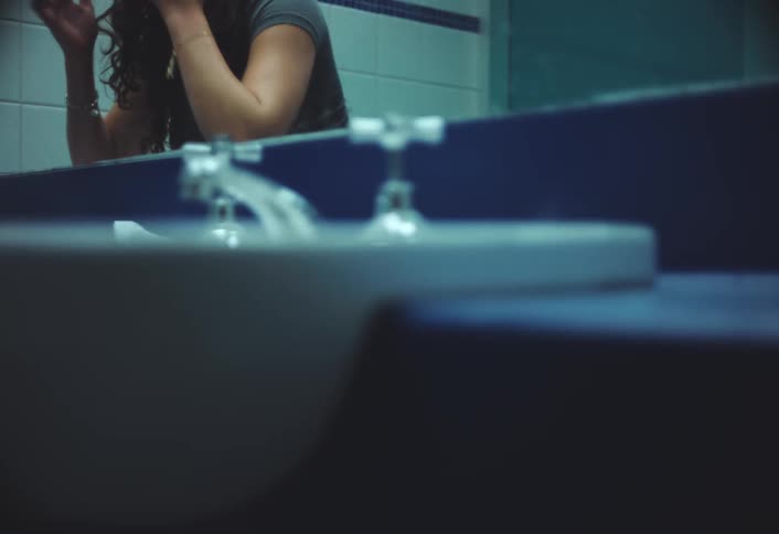 A young woman is fixing her hair in a bathroom mirror