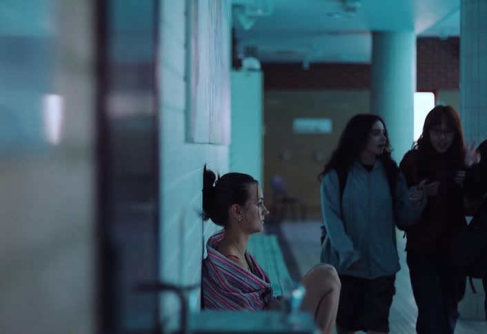 Girl sitting on the ground with a cloth over her shoulders she is very sad next to her 3 girls pass by talking to each other and they dont consider her