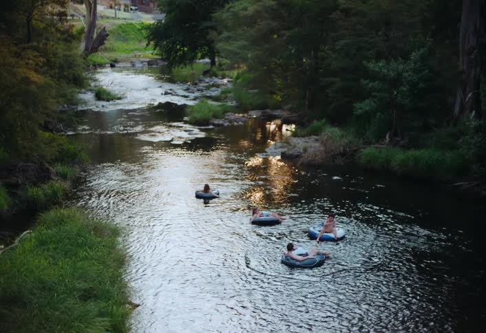 A group of friends floats on round inflatable rings on a calm river in the evening