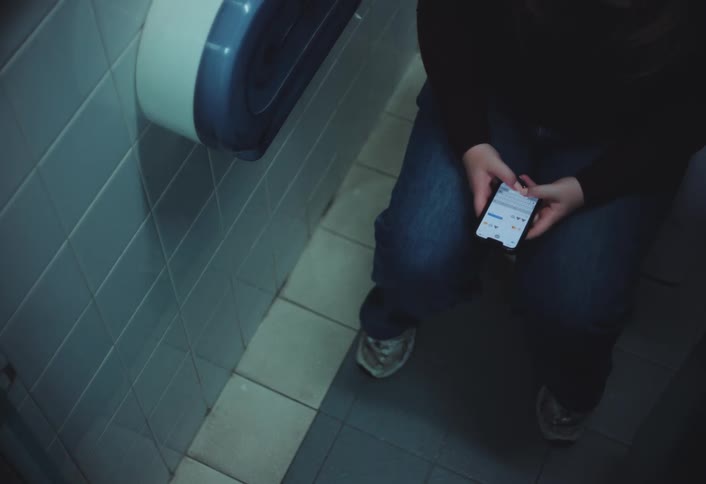 Boy typing on a cell phone while sitting in the bathroom