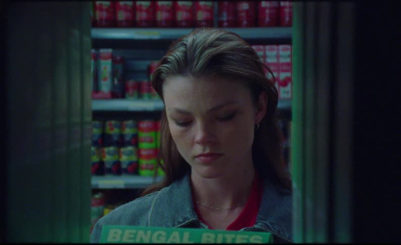 A female customer wearing a denim jacket picks up a box off the shelf in a grocery store looks at it and then turns her head to the right