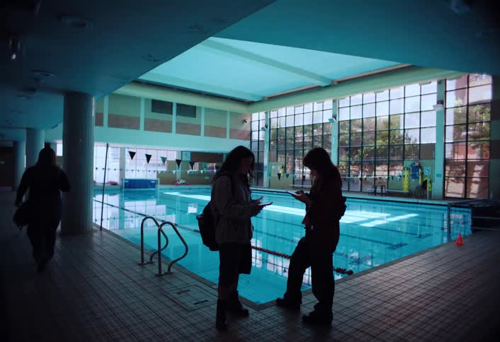 People using smartphones while standing next to a swimming pool indoors