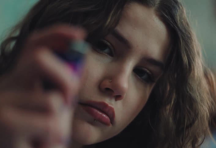 Close up of a teenage girl with wavy hair looking directly at the camera chewing bubblegum while igniting a lighter