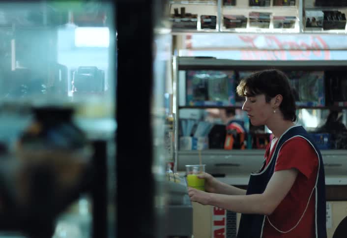 A store clerk takes a break browsing their phone while sipping a green frozen slushy beverage