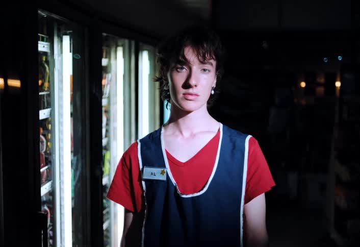 A store employee closes a glassdoor refrigerator while looking at the camera as the stores lights flicker and begin to go out