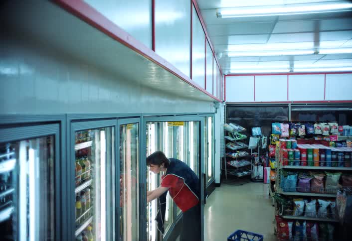 A worker in a welllit store restocks two gallon jugs of milk in the refrigerated section