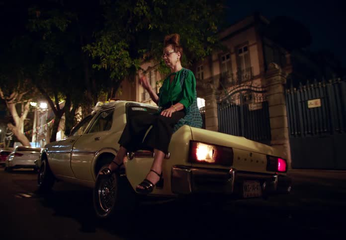 A woman is sitting on a car on a street in the city