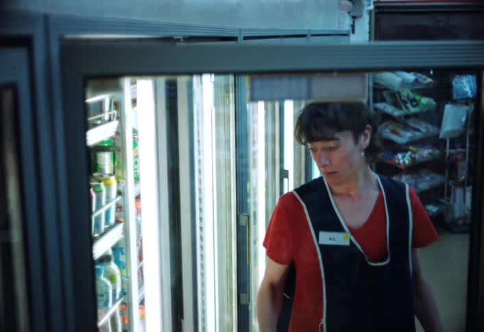 A store clerk restocks a fridge with gallon sized milk containers in a store