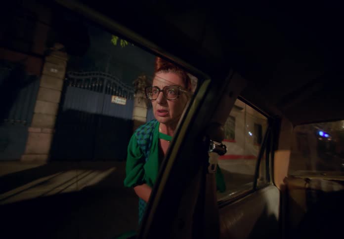An elderly woman appearing frantic tries to open the doors of her locked car after leaving the keys inside set against the backdrop of a city at night