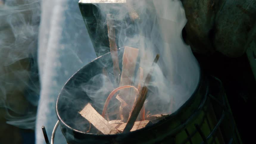 Wood shavings and scraps inside a metal bucket smolder with smoke rising from an unseen fire