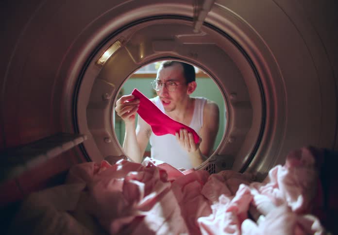 A man is upset as he looks through his laundry and sees a red sock turned his clothes pink