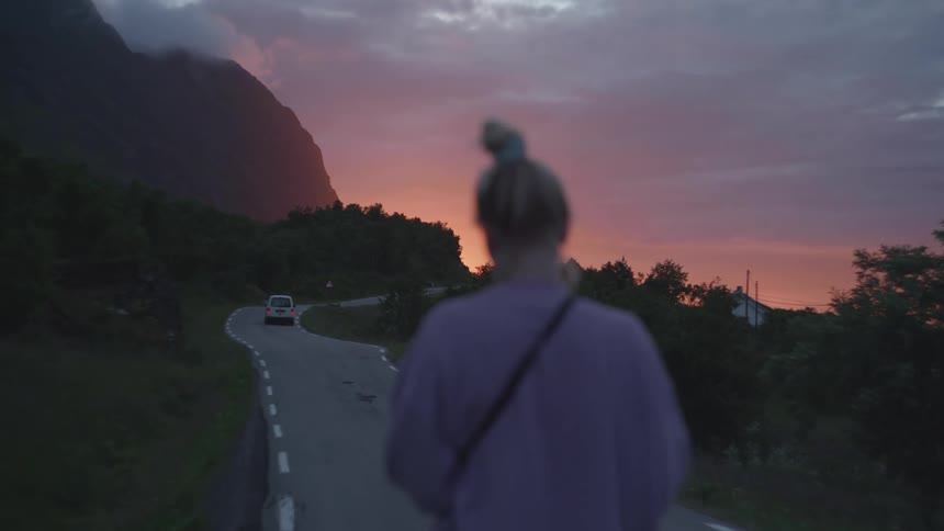Back view of a woman walking on a road at dawn surrounded by mountains