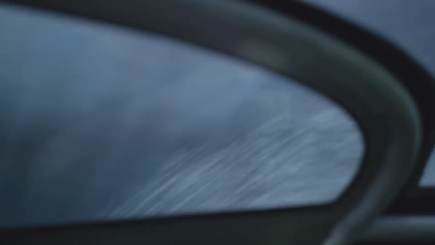 Spray of water flying through the air is seen in the small mirror of a vehicle during the day