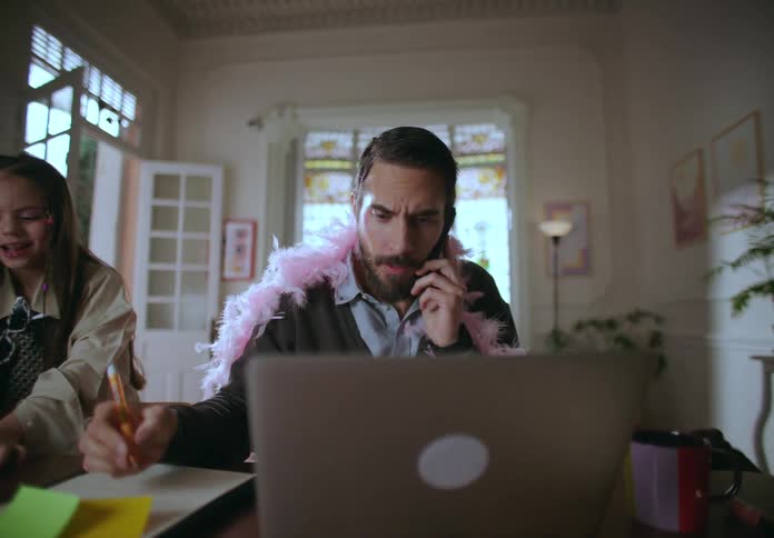 Dad trying to work on the pc but is disturbed by daughters who want to play with him and make up and dress him up with toys