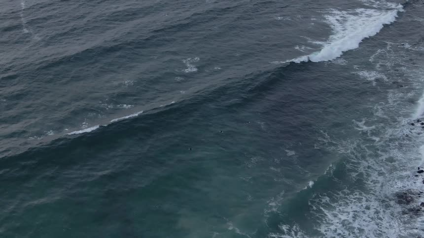 An aerial view of waves rolling onto a rocky shoreline with the waters texture and movement visible