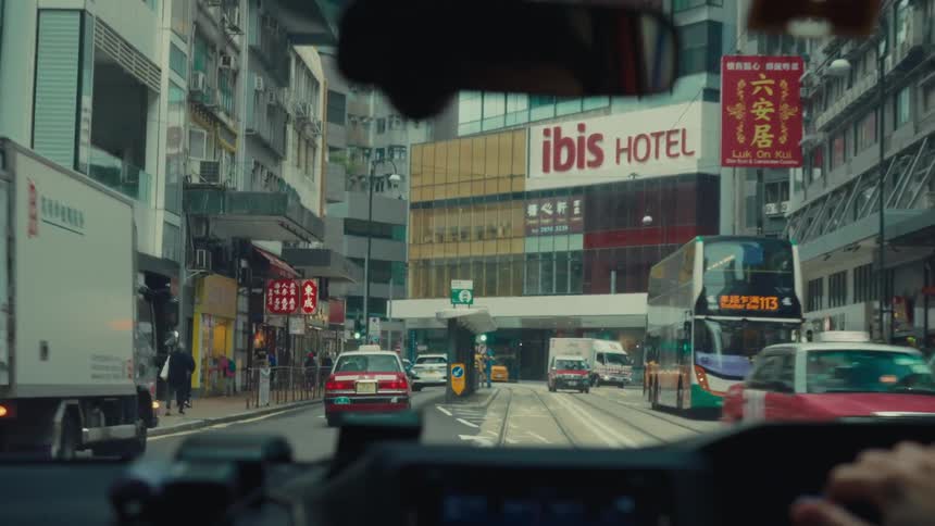 A view from inside a vehicle shows busy hong kong streets with traffic buildings and an ibis hotel sign