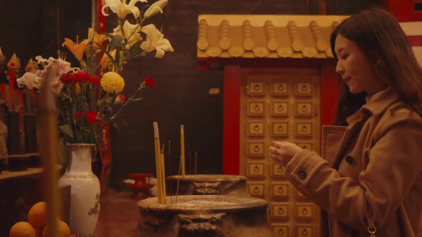 A woman prays as she carefully places lit incense sticks on an altar in a traditional asian temple