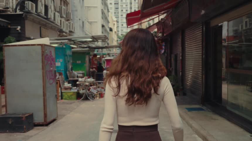 A woman walks on an alleyway lined with street shops and residential buildings