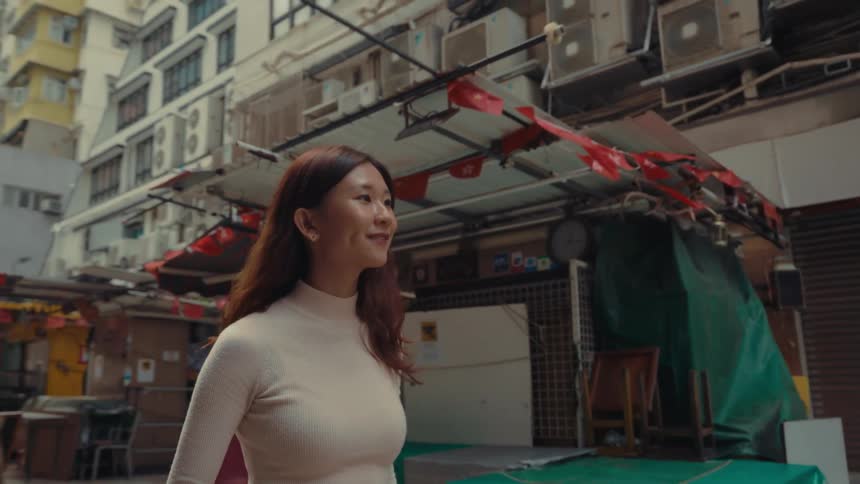 Woman and other pedestrians walk along a city street lined by stores and standalone food booths during the daytime
