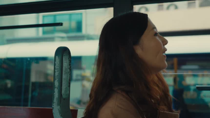 A chinese woman on a doubledecker tram in hong kong smiles and takes a photo with a disposable camera while another tram passes outside the windows