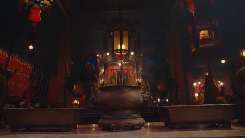 The interior of hong kongs man mo temple featuring large lit incense burners and traditional hanging lanterns all surrounded by a soft glow and people evokes an aura of reverence