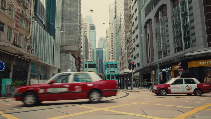 A bustling hong kong street scene unfolds with iconic red taxis and blue doubledecker trams navigating through an intersection as pedestrians are seen walking by on the sidewalks