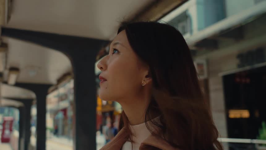 Closeup of woman standing at a hong kong tram station gaze shifting as her expression subtly changes and strands of dark hair moved gently by a breeze offering a clear picture of city life engagement