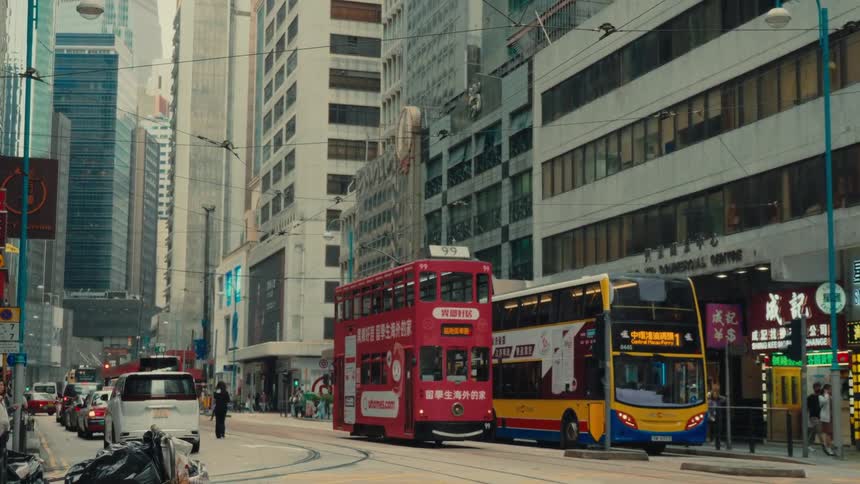 A busy hong kong thoroughfare shows off a standstill traffic scene that features a signature duallevel tram and bus amidst towering buildings while people casually traverse the sidewalks alongside