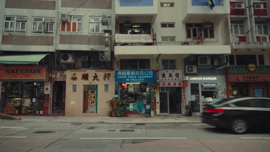 Vans drive down a street past buildings that have stores and apartments