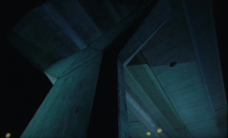Looking upwards to reveal the underneath of a substantial concrete highway overpass the view highlights its large support structure and the expansive expanse of the road surface seen up above at night time