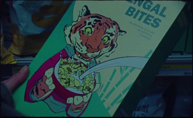 A box of cereal labeled bengal bites featuring a cartoon tiger held in front of a grocery store shelf stocked with various snacks