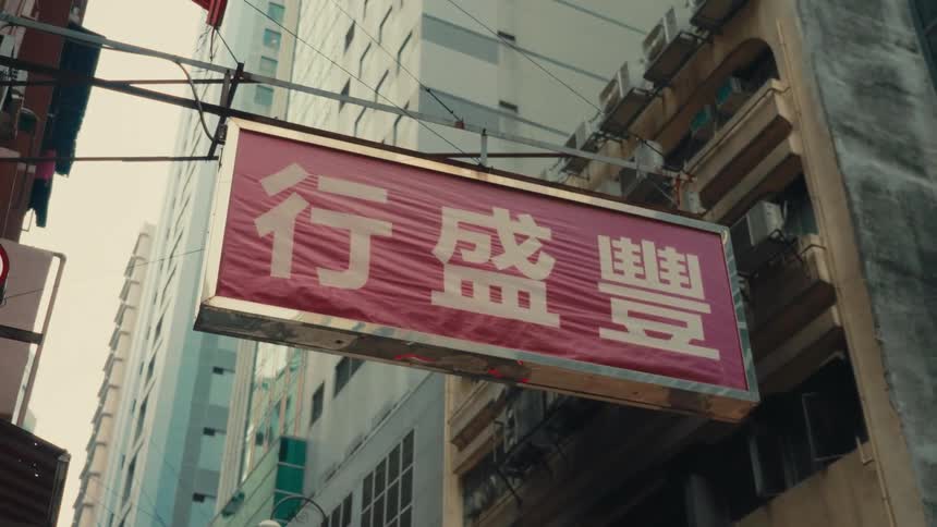 Looking upwards at a weathered red rectangular business banner adorned with large white traditional chinese calligraphy prominently suspended and displayed above the thoroughfare in a hong kong street
