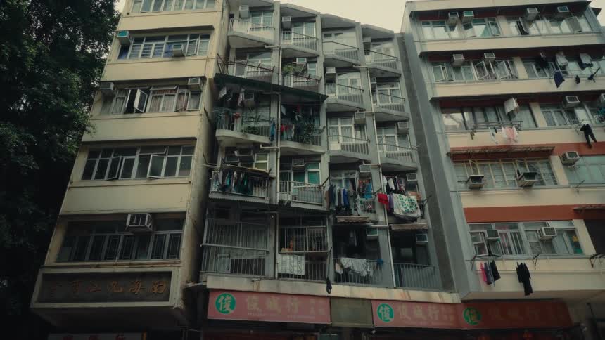 A view of a hong kong tong lau residential structure displaying cramped balconies and closelypacked windows offers insight into urban life as a red doubledecker bus passes