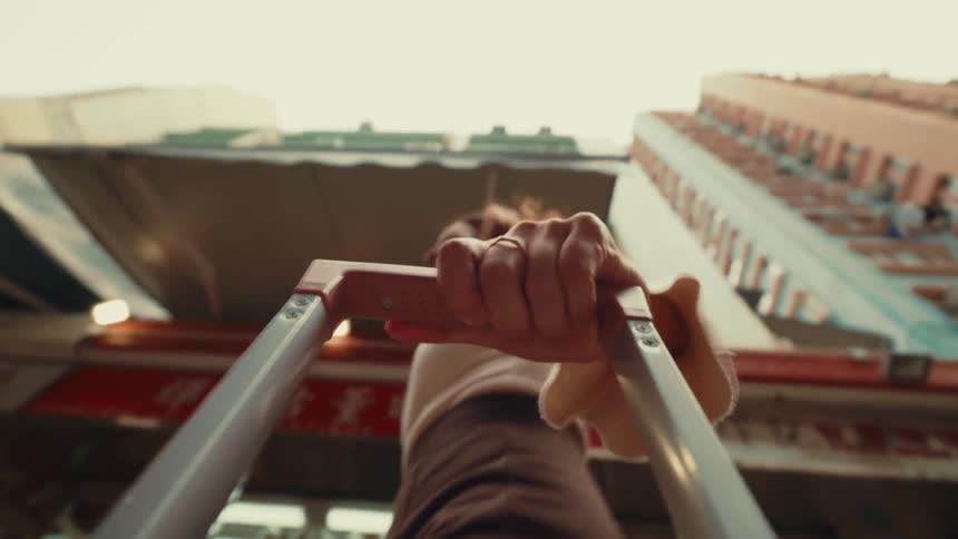 POV from the suitcase looking up at a young woman holding the luggage handle and pushing it along as she walks in the city.