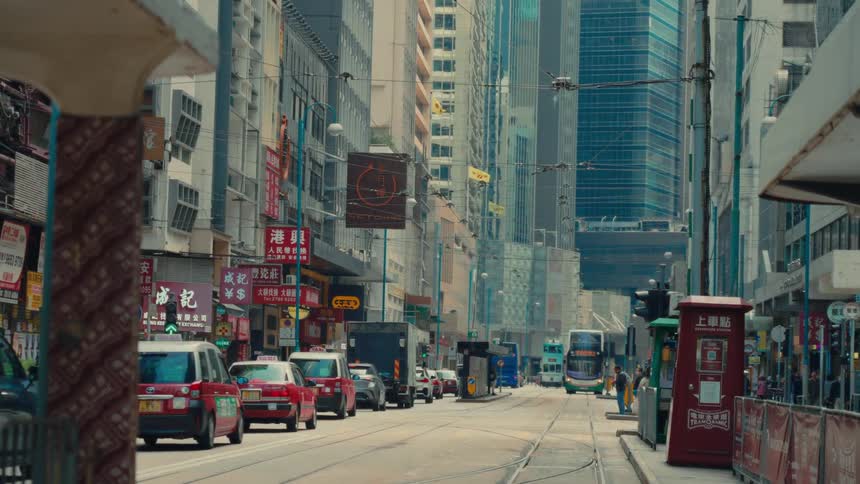 A busy hong kong street scene shows red taxis and a doubledecker bus driving along a road lined with buildings and shops