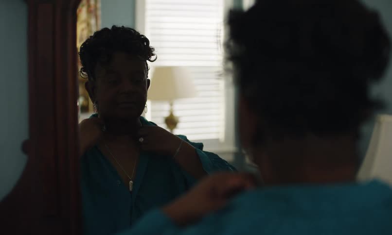 Woman from the back mirroring and adjusting her shirt and necklace