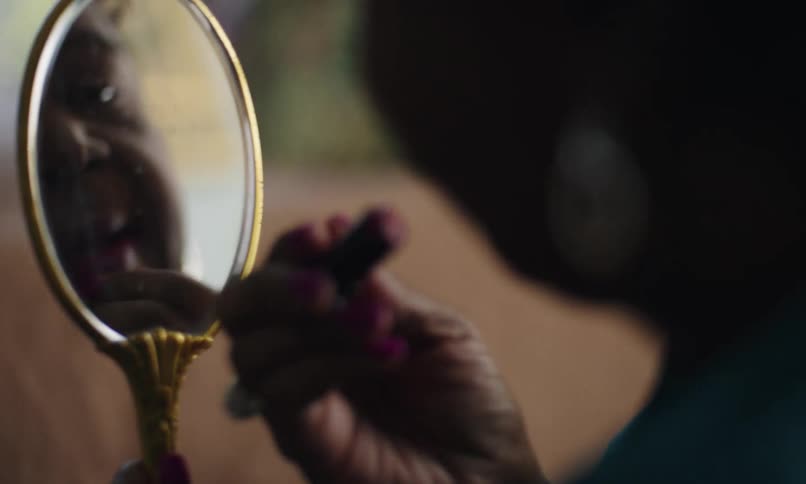 Woman applying pink lipstick in front of a small mirror