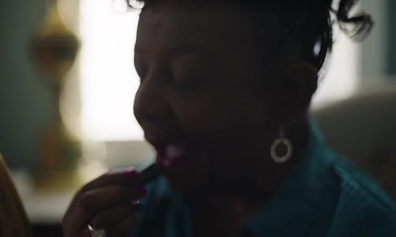 A black woman applies lipstick and rubs her lips together