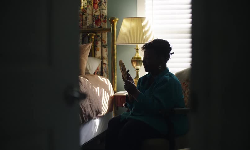 A woman is using a small mirror to put on lipstick
