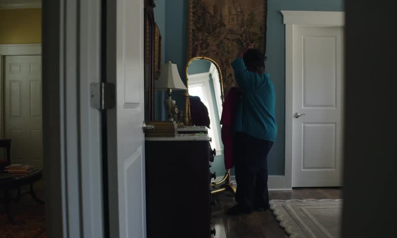 Woman in a room of the house holding a pink outfit and looking at herself in front of the mirror