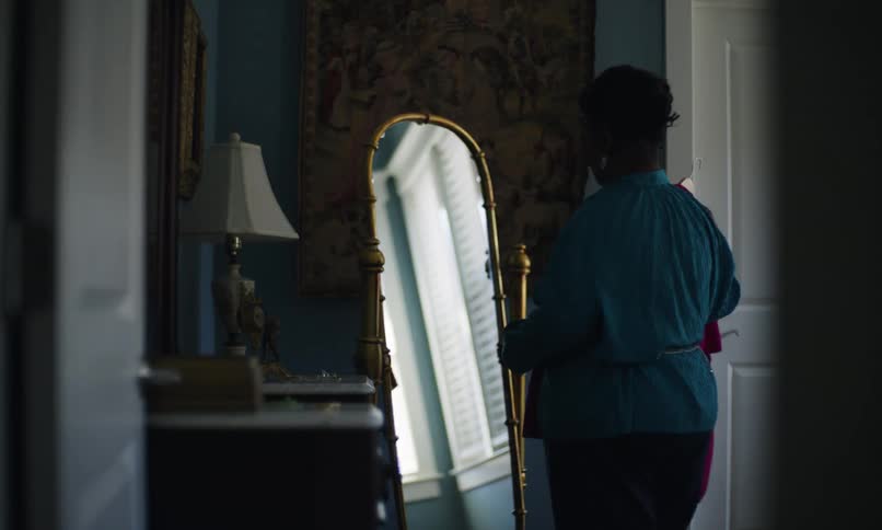 Woman looking at herself in the mirror with a dress in her hand as she dances contentedly