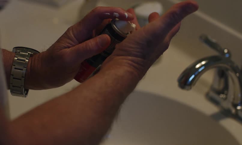A man shakes a can to get more shaving cream out of it in a bathroom