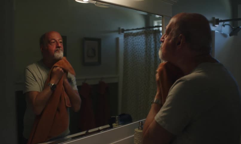 A man is washing his face with a towel in front of the mirror