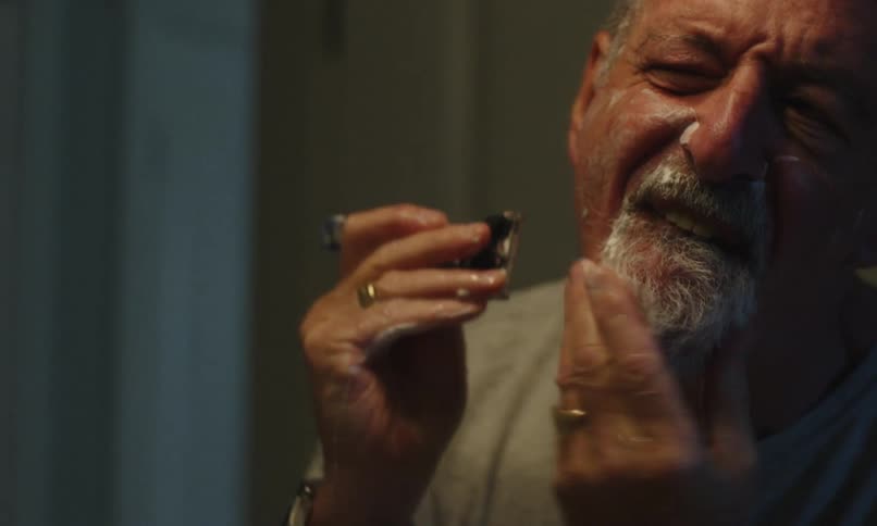 Elderly man shaving his beard in the bathroom mirroring himself