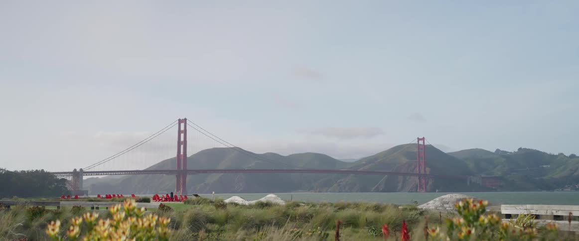 The golden gate bridge is seen in the distance spanning across water with hills visible beyond under a hazy sky
