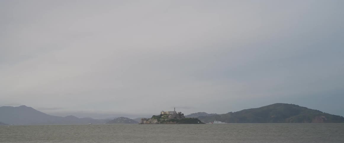 Alcatraz island sits in the middle of san francisco bay surrounded by water and under a cloudy overcast sky a historic landmark