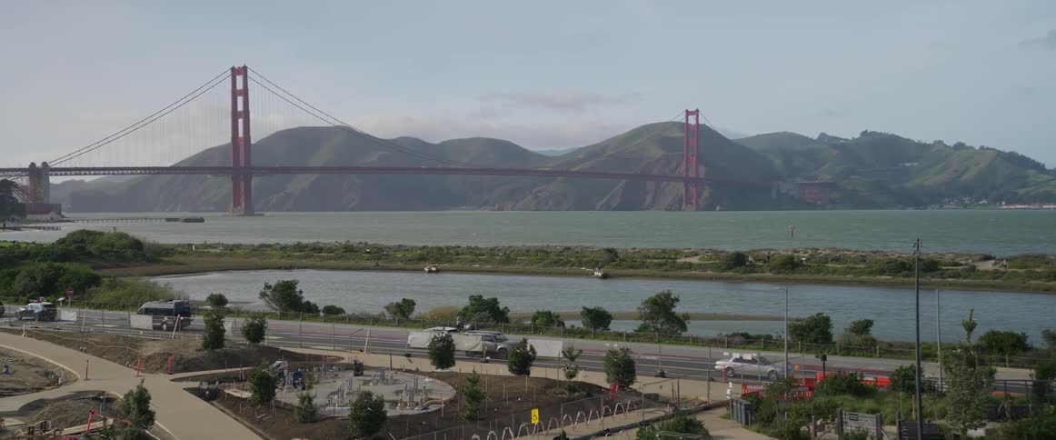 A view of san franciscos iconic golden gate bridge spans across the bay connecting to the marin headlands while cars and a bus traverse on the road in the foreground below under a grey sky
